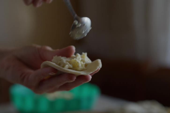 Close-up slow motion of hands spooning a mashed potato filling onto dough and pinching it shut to make a homemade pierogi