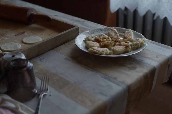 A plate of delicious homemade pierogi sits on a rustic table next to a rolling pin and uncooked dough