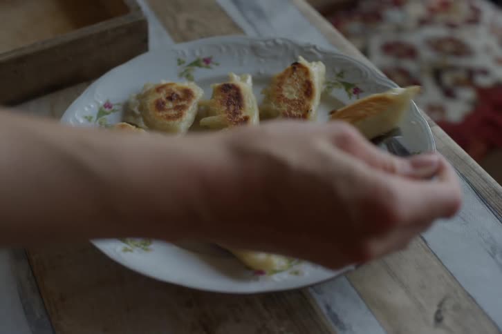 A person places freshly fried pierogi onto a vintage floral plate on a rustic table