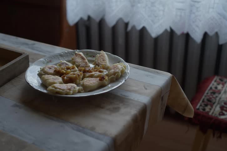A plate of freshly fried traditional Polish pierogi with onion topping sits on a dining table by a window