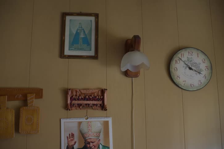 A static shot of a vintage-decorated wall with religious icons, a clock, and a lamp