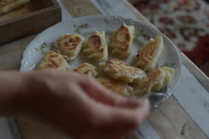 A person uses a fork to arrange freshly pan-fried pierogi dumplings on a decorative plate