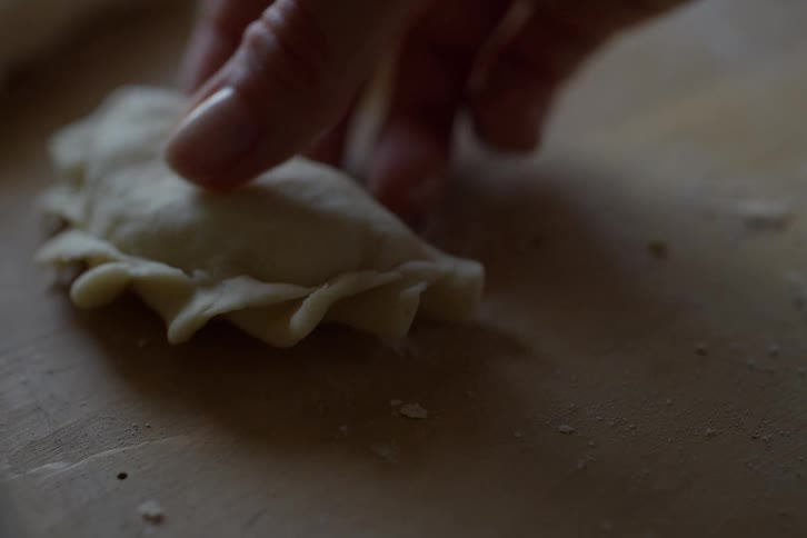 A close-up slow-motion view shows a hand delicately placing a handmade dumpling on a floured wooden surface