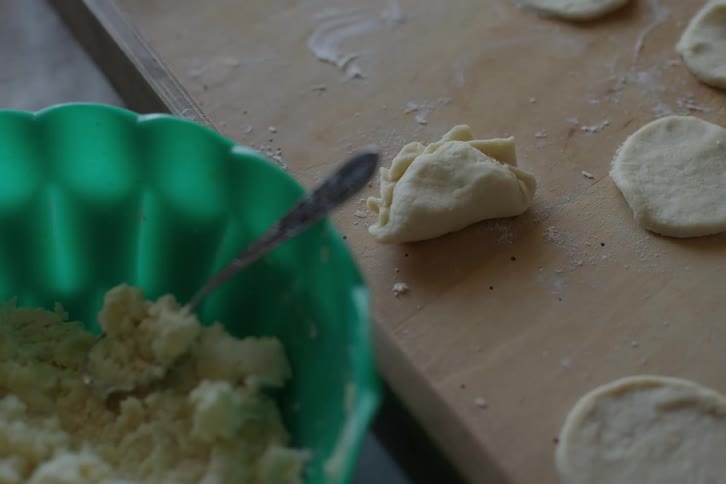 Close-up of a woman's hands preparing homemade vareniki, folding the dough over potato filling on a wooden board