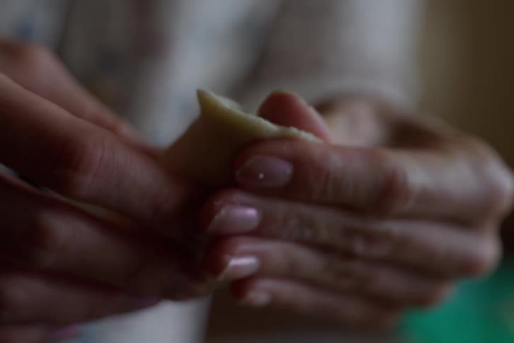 A macro shot shows a person's hands carefully molding and folding dough to make a traditional dumpling