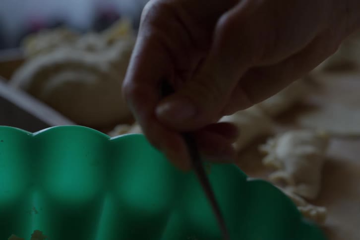 A close-up of a person's hand using a spoon to scoop filling from a green bowl to make homemade dumplings