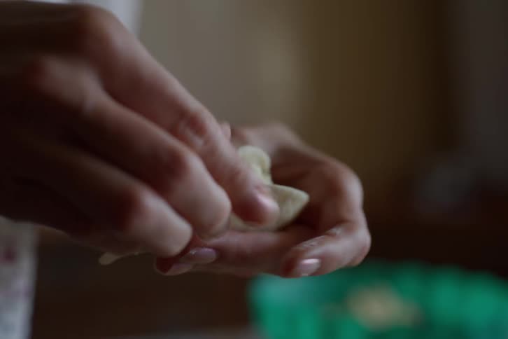 A slow motion close up of a woman's hands carefully pinching the edges of a homemade dumpling to seal it