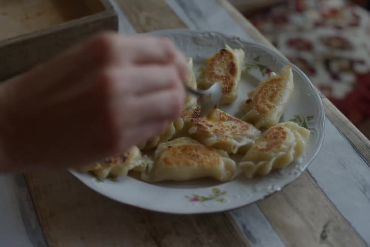 A person adds a fried onion topping to a plate of traditional Polish pierogies sitting on a rustic table