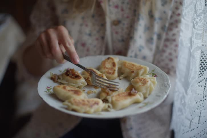 Close-up slow-motion shot of a person enjoying a plate of traditional fried pierogi with onions