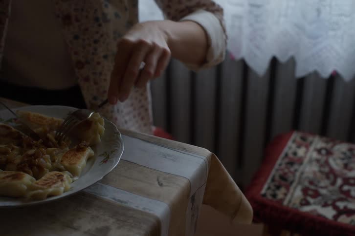 A woman uses a knife and fork to eat a plate of traditional dumplings topped with fried onions