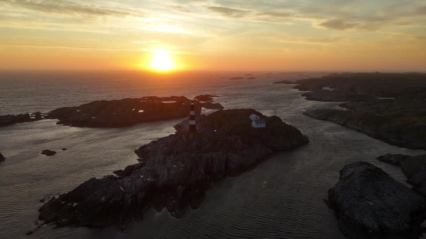 A stunning aerial view captures a red and white lighthouse on a rocky island during a magnificent sunset over the ocean