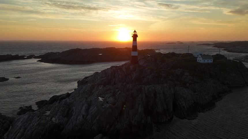 Stunning aerial view of a red and white striped lighthouse on a rocky island during a magnificent sunset over the ocean