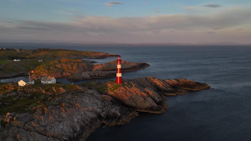 A beautiful red and white striped lighthouse stands on a rugged, rocky coastline as the sun sets, casting a warm golden light over the landscape