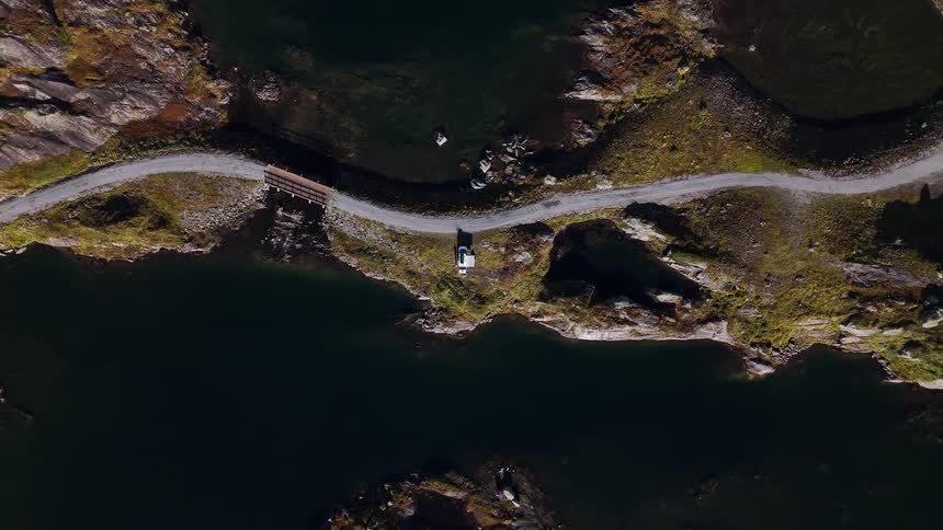 Aerial top-down view of a camper van parked on a remote road that weaves through beautiful, rocky mountain lakes