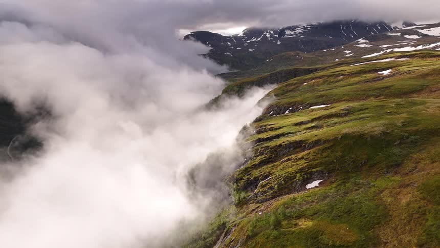 An aerial view pulls back over a stunning mountain landscape as thick clouds fill the deep green valley