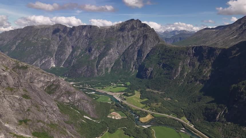 An incredible static aerial view of the majestic Trollveggen mountains in Norway, with a river and highway snaking through the lush green valley below