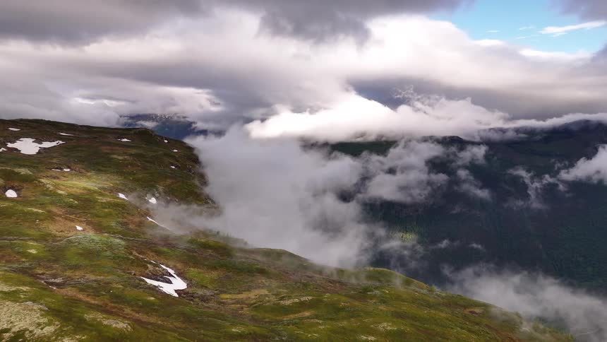 An epic static view from a mountainside as thick clouds and fog drift through a vast, green valley below