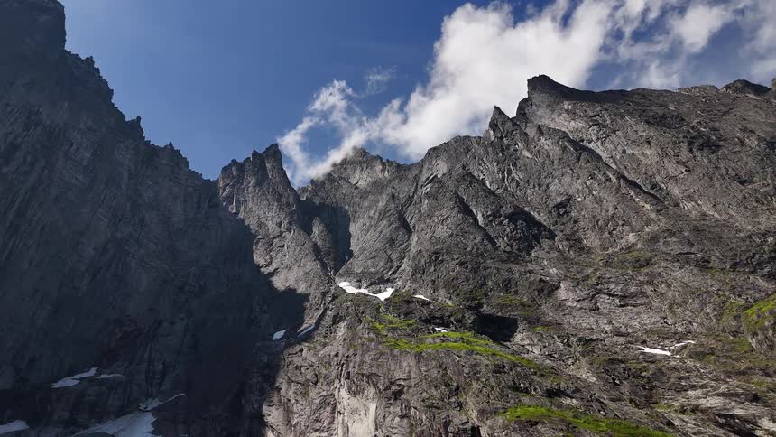 A beautiful timelapse looking up at a majestic, rugged mountain range with clouds drifting across the deep blue sky