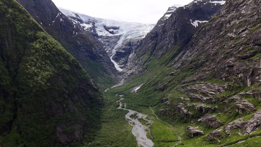 A stunning aerial perspective of the Bøyabreen glacier in Norway, majestically nestled between towering green mountains with its meltwater river below