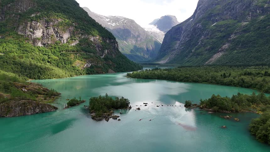 An aerial view of kayakers paddling on a stunning turquoise glacial lake surrounded by majestic mountains and a distant glacier