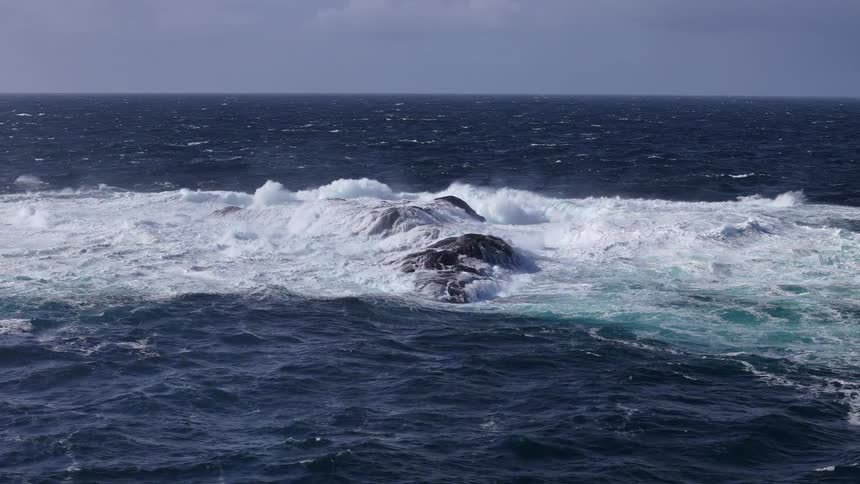Dramatic slow-motion view of large, powerful ocean waves crashing over dark rocks in a turbulent sea