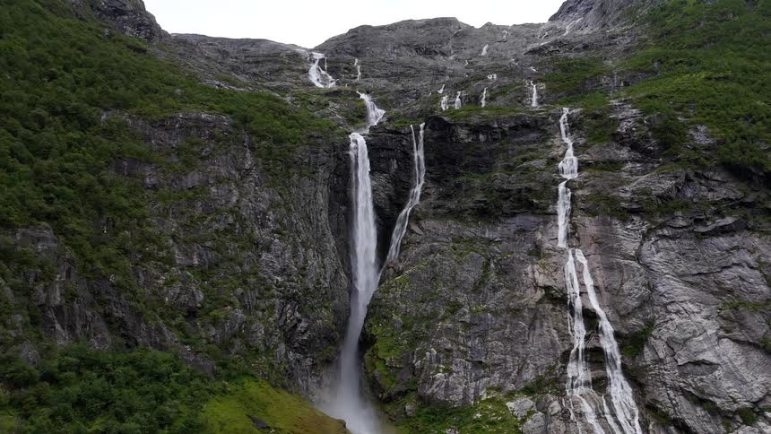 A series of powerful waterfalls cascade down a steep, rocky mountainside covered in lush green vegetation