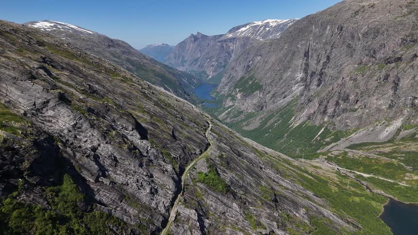 Static aerial view from the Trollstigen road showcases the stunning, vast mountain valley with a distant lake in Norway