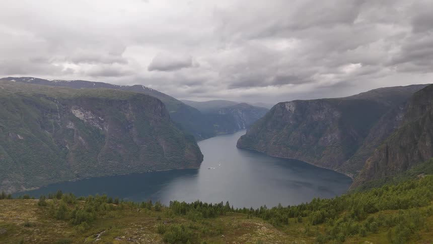 An epic aerial reveal of a lone hiker in a yellow jacket admiring the breathtaking view of a Norwegian fjord from a high mountain vantage point