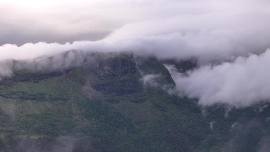 A serene yet powerful view of clouds blanketing the top of a rugged green mountain