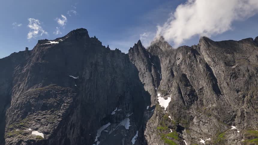 A slow aerial zoom out reveals the immense scale of a rugged, rocky mountain range under a partly cloudy sky