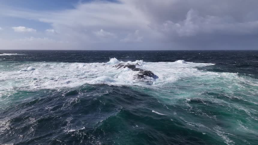 Dramatic slow motion shot of powerful ocean waves crashing over rocks under a stormy sky