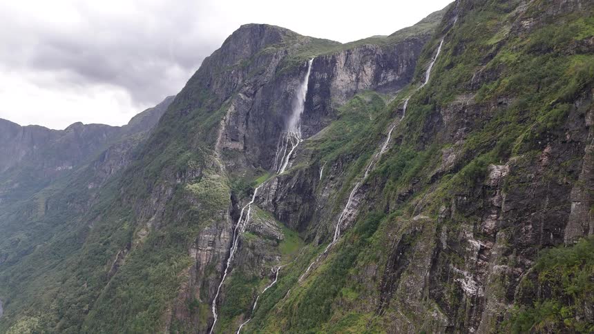 A breathtaking wide shot of multiple stunning waterfalls flowing down the steep, green cliffs of a majestic mountain