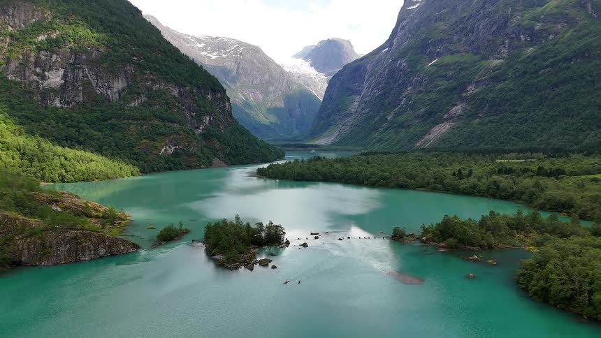 A majestic aerial view shows kayakers paddling on the stunning turquoise waters of a lake surrounded by towering mountains and a distant glacier in Norway
