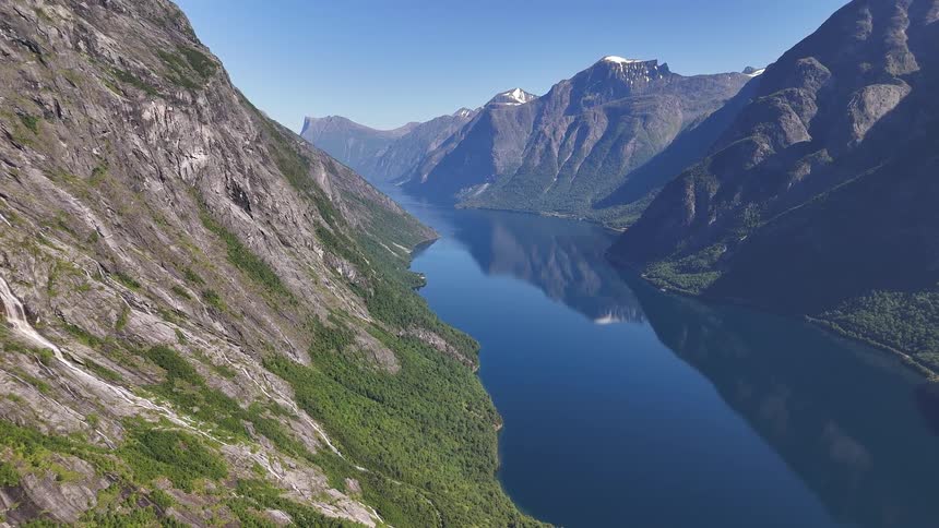 An awe-inspiring aerial view of a pristine Norwegian fjord reflecting the majestic mountains under a clear blue sky