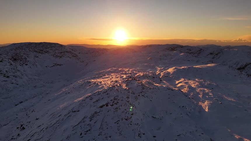 An epic aerial view of a majestic snow-covered mountain range during a stunning golden winter sunset