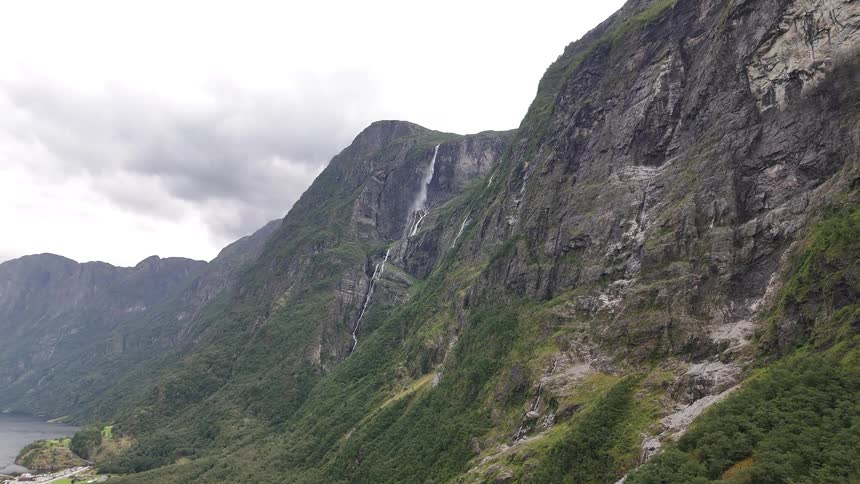 A breathtaking aerial view reveals a towering waterfall cascading down a sheer rock face in a majestic mountain range