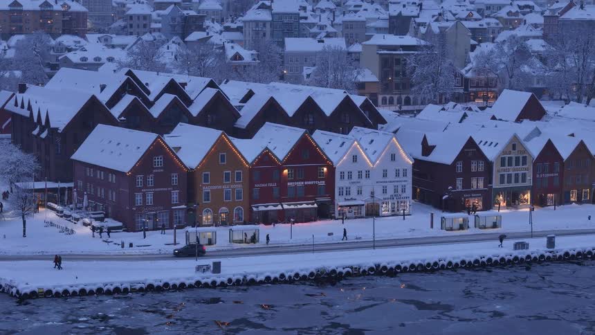 A scenic view of the colorful, snow-covered historic Bryggen wharf in Bergen, Norway, during a peaceful winter evening