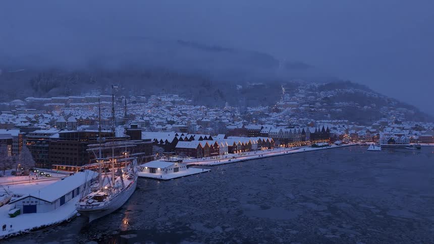 An enchanting aerial view of a historic snow-covered port city with its frozen harbor and glowing lights at twilight