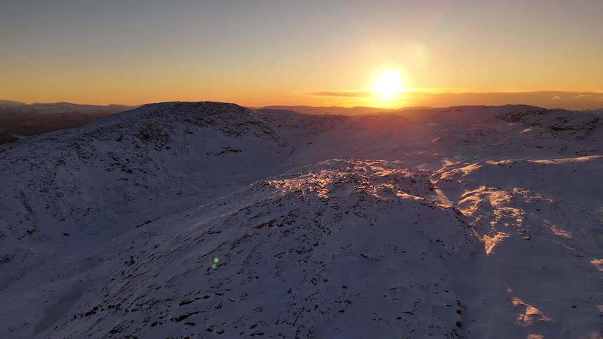 A breathtaking static aerial view captures the golden sunset over a vast, snow-covered mountain range