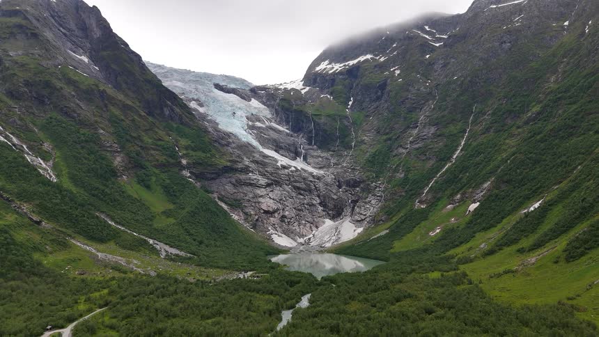 A stunning wide aerial view of a massive glacier and waterfalls cascading down lush green mountains into a serene glacial lake