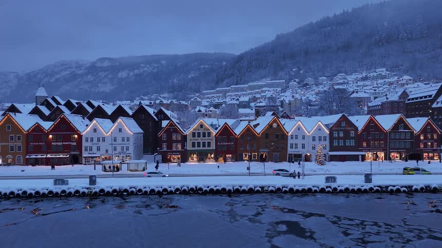 An aerial dolly shot reveals the iconic Bryggen wharf in Bergen, Norway, beautifully decorated for Christmas during a snowy winter evening