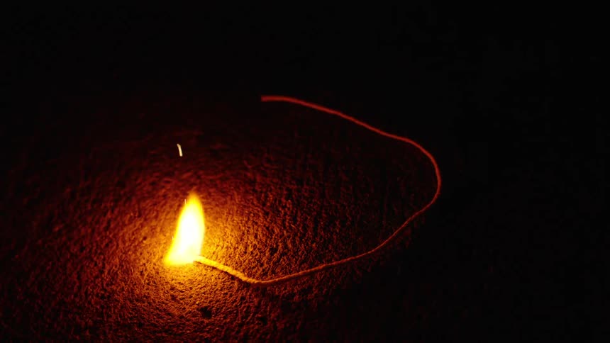 A sputtering fuse is lit by a lighter and burns with bright sparks in slow motion against a dark background