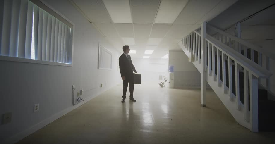 A businessman in a suit carries a briefcase and walks in slow motion through a stark, empty white room
