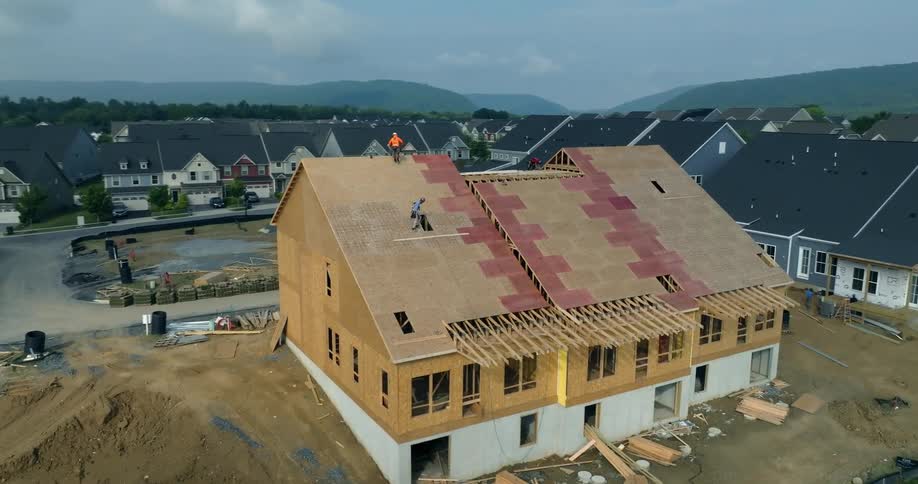 Aerial view of construction workers installing plywood sheathing on the roof of a new townhouse development