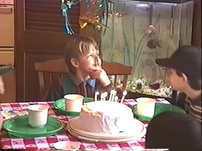 Vintage home movie footage shows a young boy sitting in front of his birthday cake before blowing out the candles