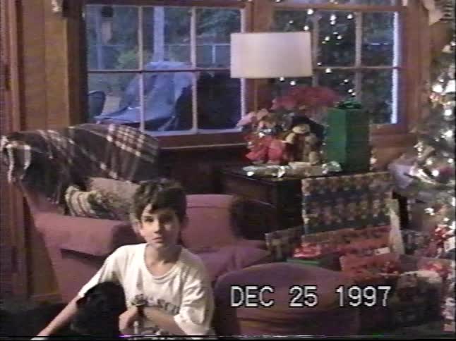A young boy pets his black dog while sitting amongst presents on Christmas morning in a 1997 home video