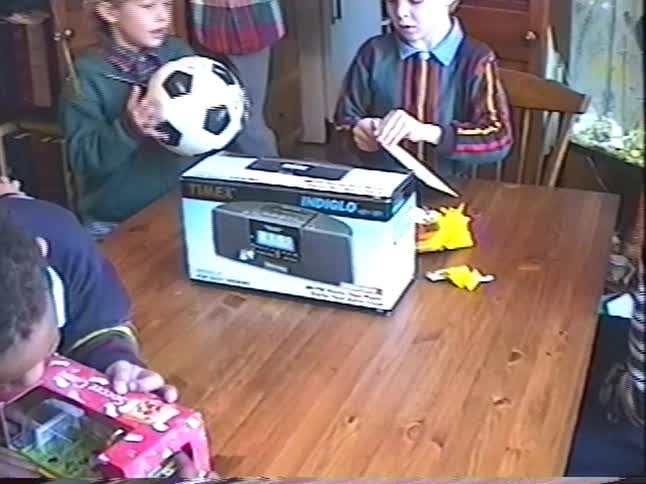 Young children gather around a wooden table at a party, excitedly looking at their new toys and gifts