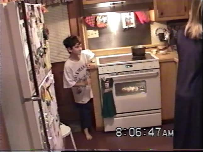 Vintage home video captures a candid moment of a young boy waiting in the kitchen as a woman prepares food