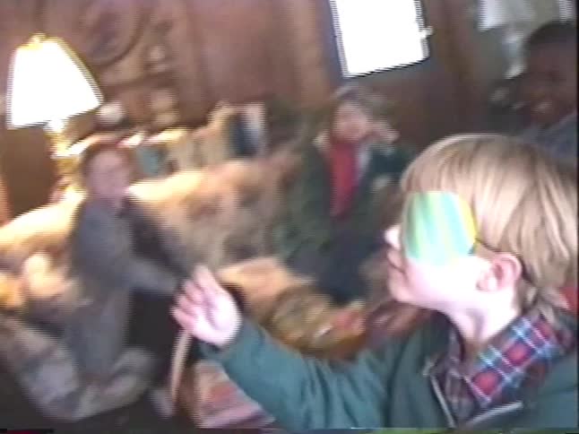 A blindfolded boy gets spun around before playing pin the tail on the donkey at a birthday party surrounded by friends and family