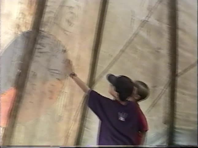 Two curious young boys explore the inside of a large teepee, examining the drawings on the canvas wall